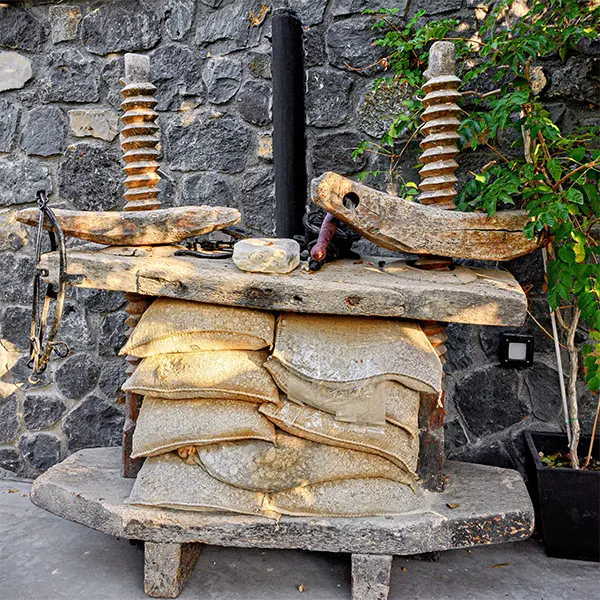 Ancient basket press in the wine tasting area next to a grey stone wall.