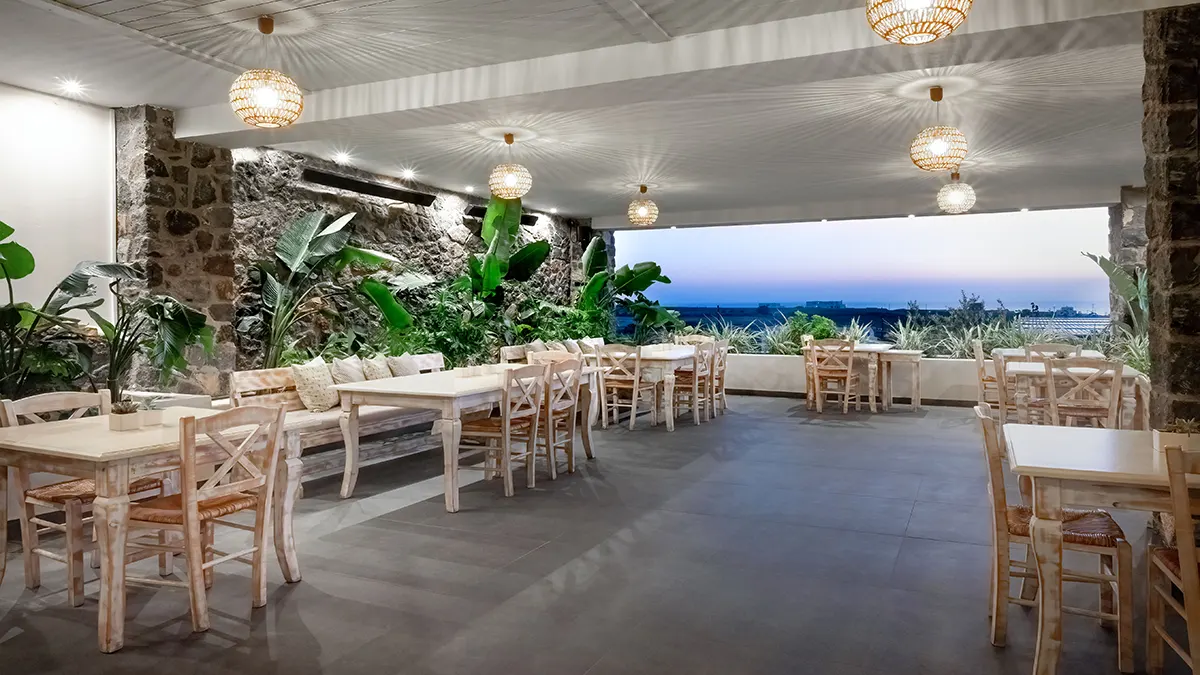 Οne of the outdoor areas of the restaurant with the table seats, low lighting and elegant decoration of plants.