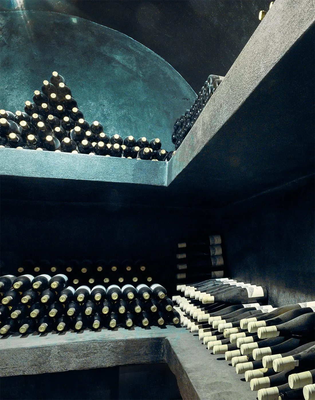 Rows of wine bottles stored horizontally on shelves in a dimly lit wine cellar.