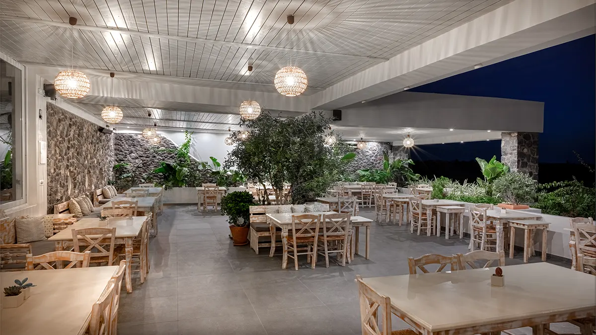 Οne of the outdoor areas of the restaurant with the table seats, low lighting and elegant decoration of plants.